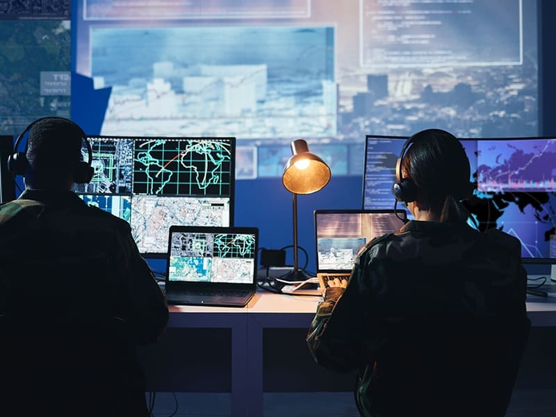 couple of people sitting at a desk in front of computer monitors