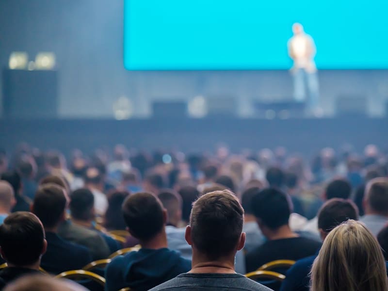 crowd of people sitting in front of a large screen