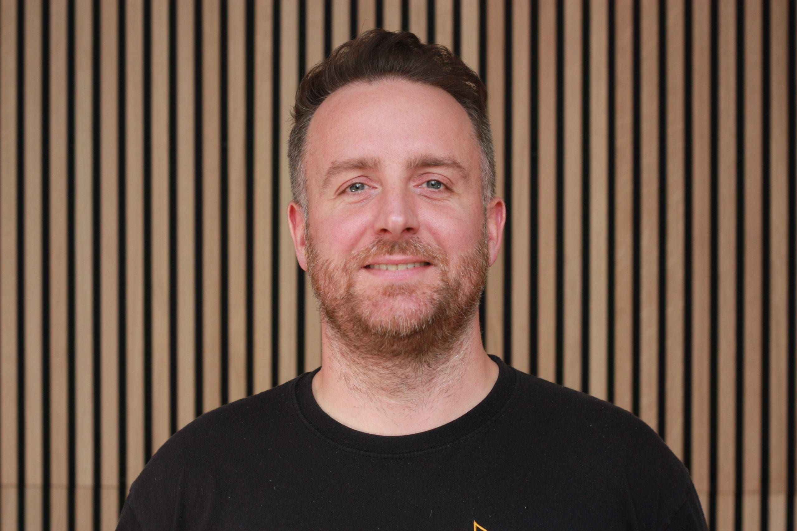 man in a black shirt standing in front of a wall